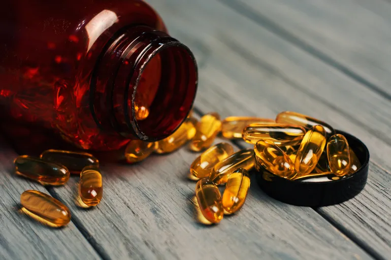 Fish oil capsules with omega 3 and vitamin D in a glass bottle on wooden texture, healthy diet pills By RomanWhale studio @ادوبي ستوك